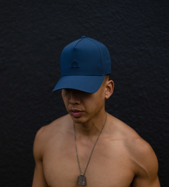 Man in an Abyss trucker cap and a silver dog tag necklace against a dark wall.
