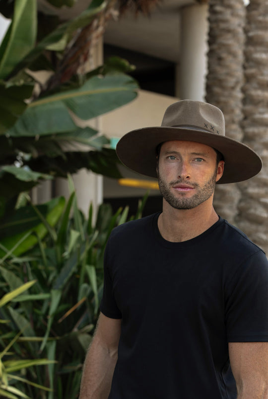 A wide-brim felt hat in Terra with a black tee among palms.