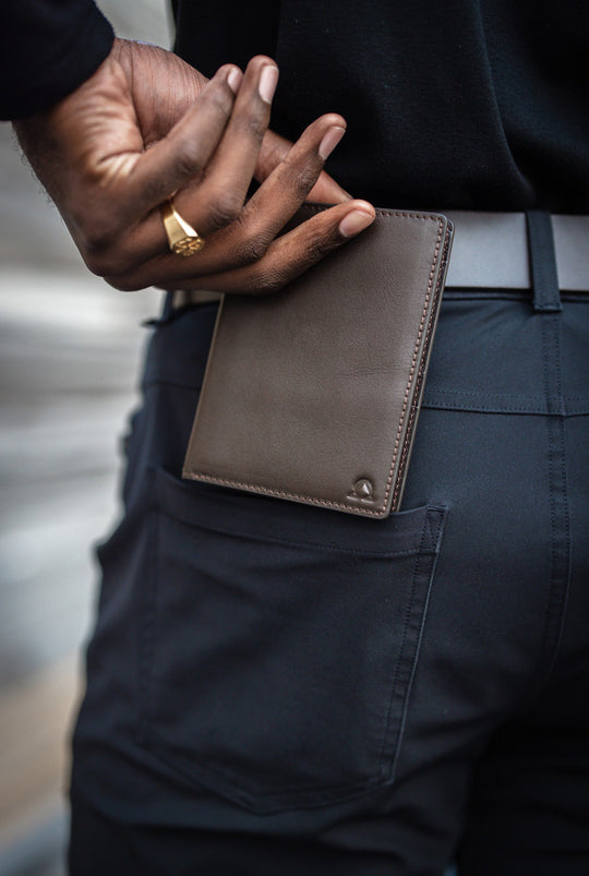 A brown wallet going into a pocket, a gold signet ring on the hand.
