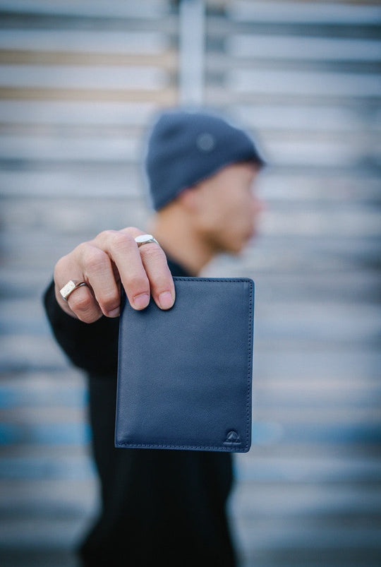 Abyss full-grain leather wallet held out to the camera, navy beanie behind.