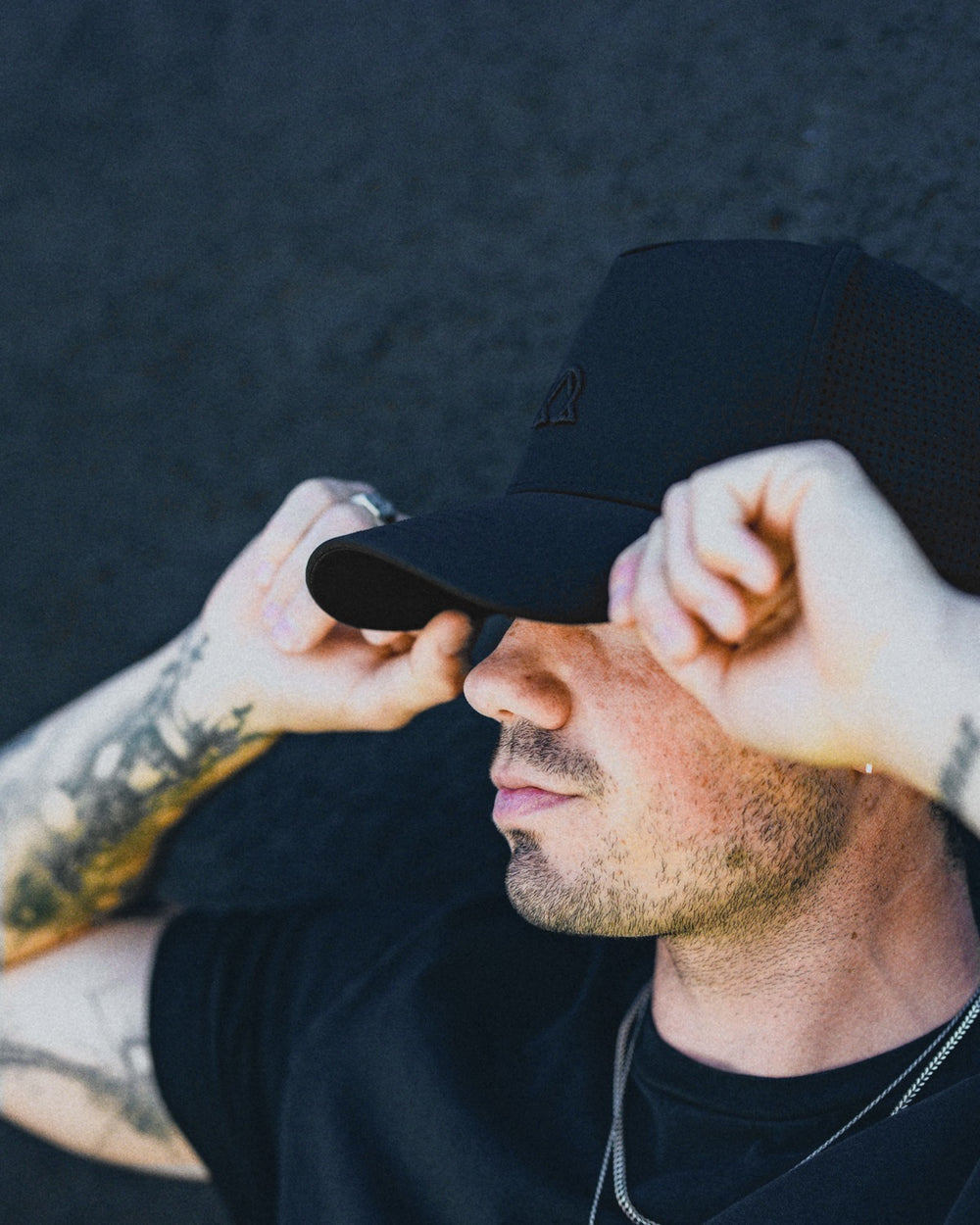 Lux Trucker hat in Onyx pulled low with both hands.