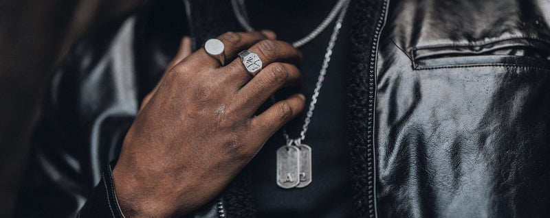 Silver signet rings and Primis Finis tags worn with a black leather jacket.