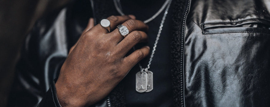 Silver signet rings and Primis Finis tags worn with a black leather jacket.