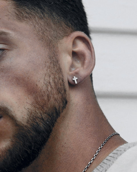 Crux cross stud earring in 925 sterling silver, worn at the ear, with a silver chain.