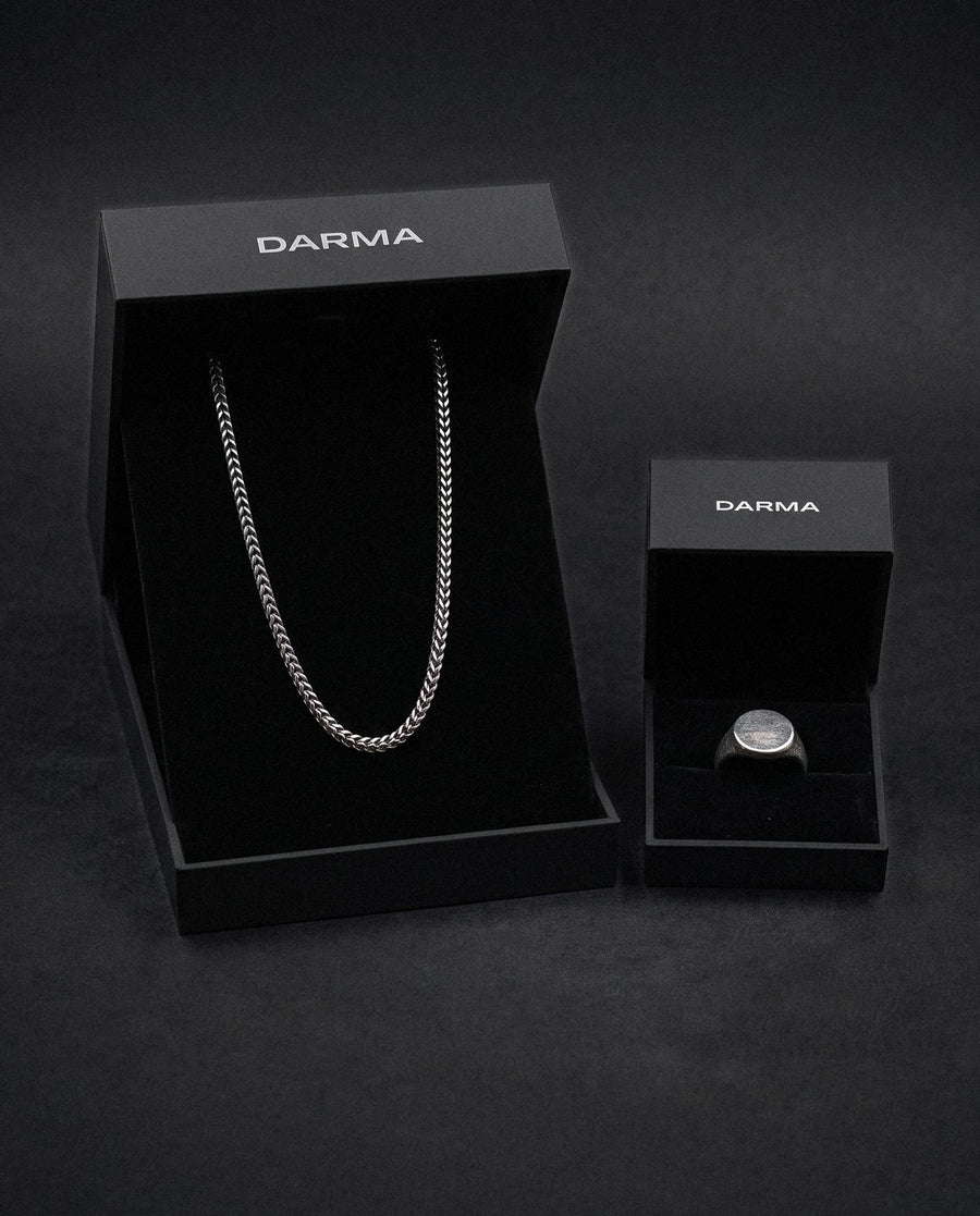 The Bond Set in 925 Silver: the Franco chain and the Aegis signet ring in 925 sterling silver, each in an open DARMA box, on a dark backdrop.