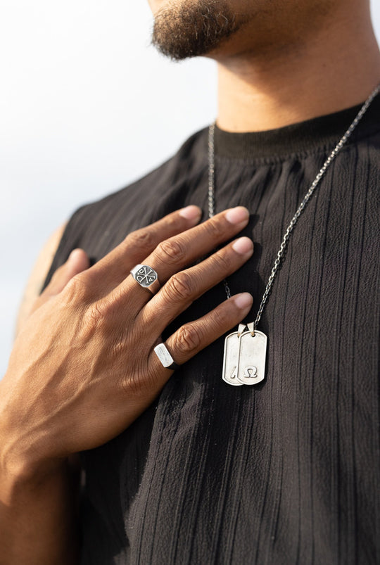 Primis Finis tags in sterling silver, a hand with two silver rings at the chest.