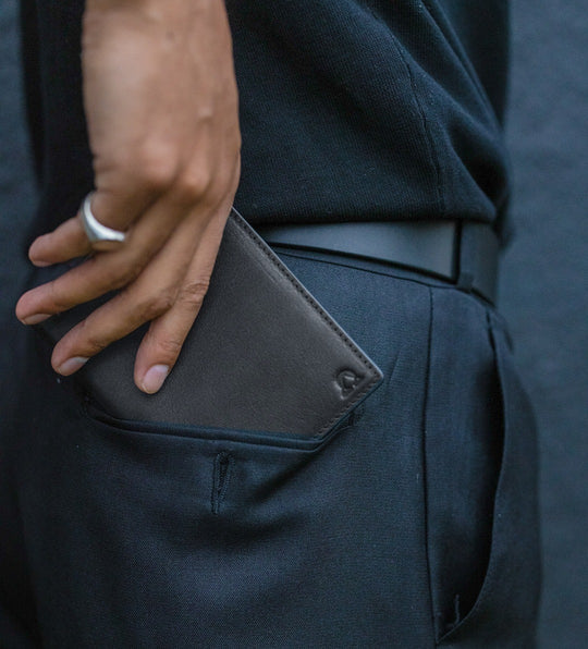 Onyx full-grain leather wallet slid into the pocket of dark trousers, a silver ring on the hand.
