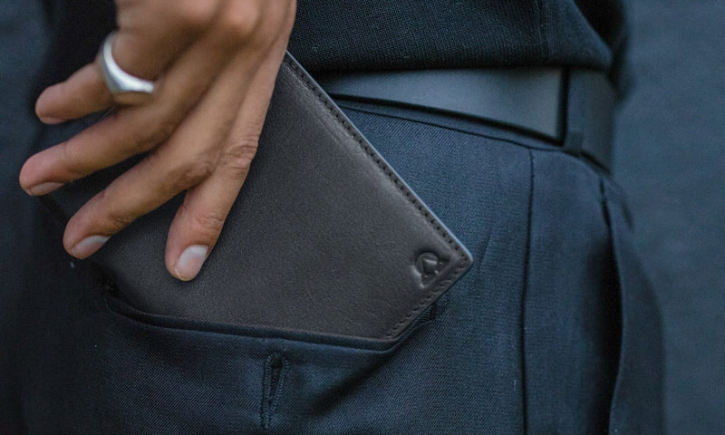 Onyx full-grain leather wallet slid into the pocket of dark trousers, a silver ring on the hand.